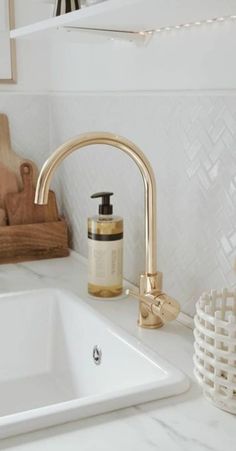 a white sink with gold faucet and soap dispenser next to it