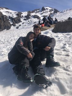 two people sitting in the snow on top of a mountain