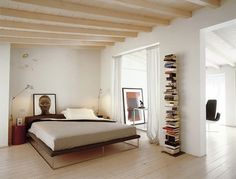 a bed sitting in a bedroom next to a tall book shelf with books on it