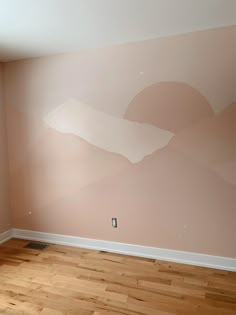 an empty room with wood flooring and painted mountains on the wall in pink tones