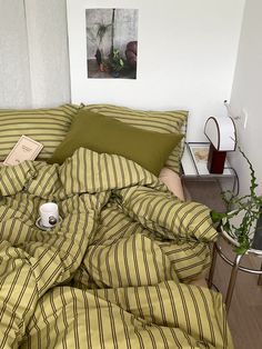 an unmade bed with green and yellow striped comforter in a small room next to a potted plant