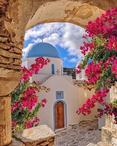 an arched doorway with pink flowers growing on it and a blue dome in the background