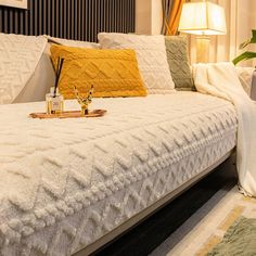 a white bed with yellow pillows on top of it next to a night stand and lamp