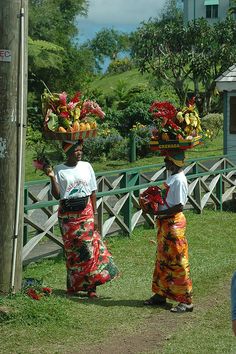 two women in colorful skirts carrying flowers on their heads