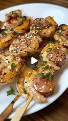 a white plate topped with meat and veggies on skewered in sesame seeds