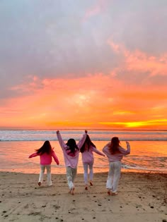 three girls are running on the beach with their arms in the air as the sun sets