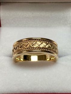 a yellow gold wedding band in a box with red velvet lining the edges and an intricate braided design