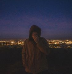 a person standing on top of a hill at night with the city lights in the background