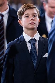 a young boy wearing a suit and tie standing next to other men in business suits