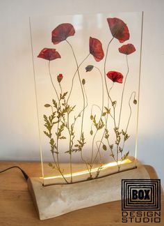 a glass vase filled with red flowers sitting on top of a wooden table next to a white wall