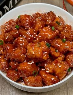 a white bowl filled with orange chicken and sesame seeds on top of a wooden table