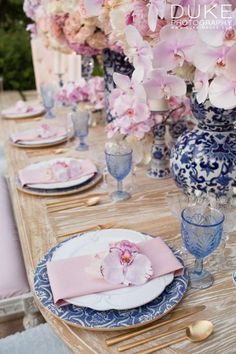 the table is set with blue and white plates, pink napkins, and flowers