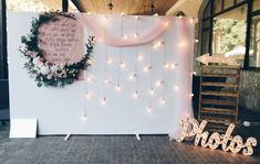 a white backdrop with lights and a wreath on it that says photos, hanging from the ceiling