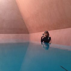 a woman taking a selfie in an indoor swimming pool with blue water and pink walls