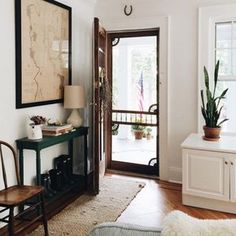 a living room with an open door and potted plants on the table next to it