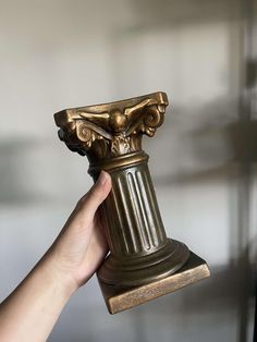 a hand holding up a golden vase in front of a white wall