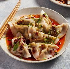 two bowls filled with dumplings covered in sauce and garnished with green onions