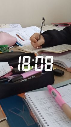 a person sitting at a desk with a book and pen in front of the clock