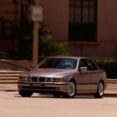 a silver car driving down a street next to a tall building with steps leading up to it