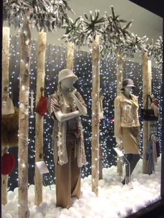 a window display with mannequins dressed in winter clothing and snow covered trees