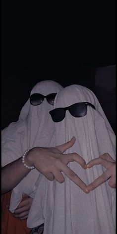 two people dressed in white are making a heart shape with their hands while wearing sunglasses