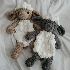 two crocheted sheep laying on top of a white bed sheet next to each other