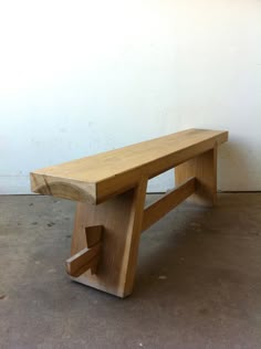 a wooden bench sitting on top of a cement floor next to a white wall in an empty room