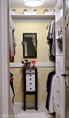 a closet with yellow and white wallpaper, drawers and clothes hanging on the walls