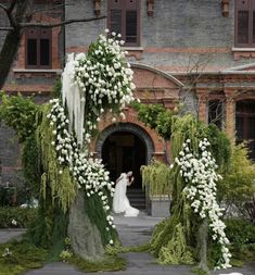 a bride and groom are standing in front of an archway with white flowers on it