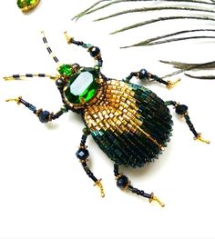 a green and gold bug brooch sitting on top of a white table next to feathers