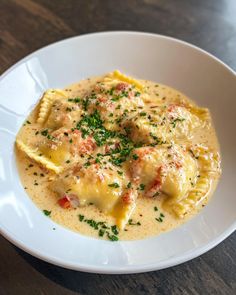 a white bowl filled with ravioli and sauce on top of a wooden table next to a fork