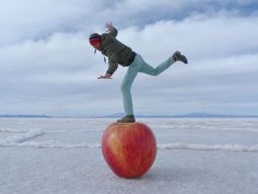 a person standing on top of an apple in the middle of snow with their arms outstretched