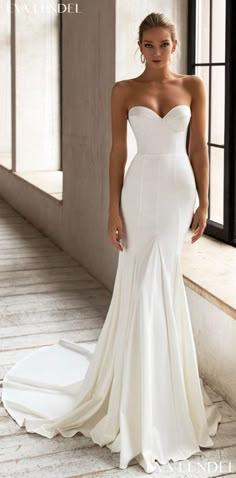 a woman in a white wedding dress standing by a window with her hands on her hips