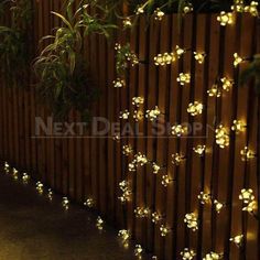 some lights that are on the side of a wooden fence and planters with plants in them