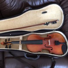 an old violin in its case sitting on a leather couch with it's lid open