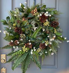 a wreath with pine cones and greenery hanging on a door