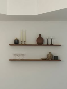 two wooden shelves with vases, candles and other items on them against a white wall