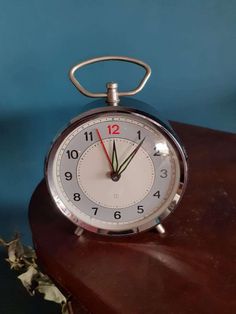 an alarm clock sitting on top of a wooden table next to a blue wall and dried flowers