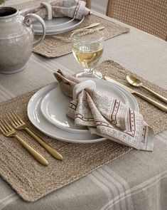 a table set with place mats, napkins and gold utensils on it