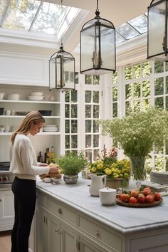 a woman preparing food in a kitchen with lots of plants and fruit on the counter