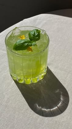 a glass filled with green liquid sitting on top of a white table covered in sunlight