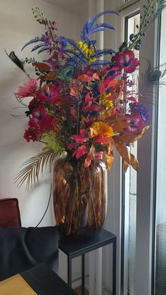 a vase filled with lots of colorful flowers on top of a wooden table next to a window