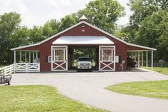 a truck is parked in front of a red barn with white doors and windows on it