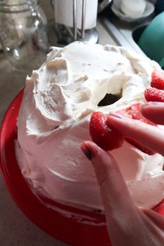 two hands reaching for a cake with white frosting and raspberries