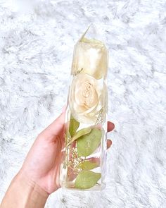 a hand holding a clear glass vase with flowers in it on a white furnishing