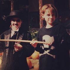 two young boys dressed up as pirates holding a wooden stick and wearing black hats, standing next to each other