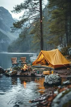 a tent set up on the shore of a lake next to some chairs and fire