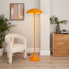 an orange floor lamp next to a white chair and potted plant in a living room