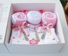 three pink and white towels in a box with spoons on the table next to it