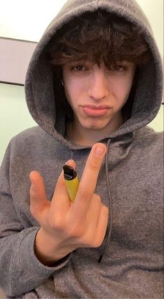 a young man wearing a hoodie and holding a small object in his hand while making the peace sign